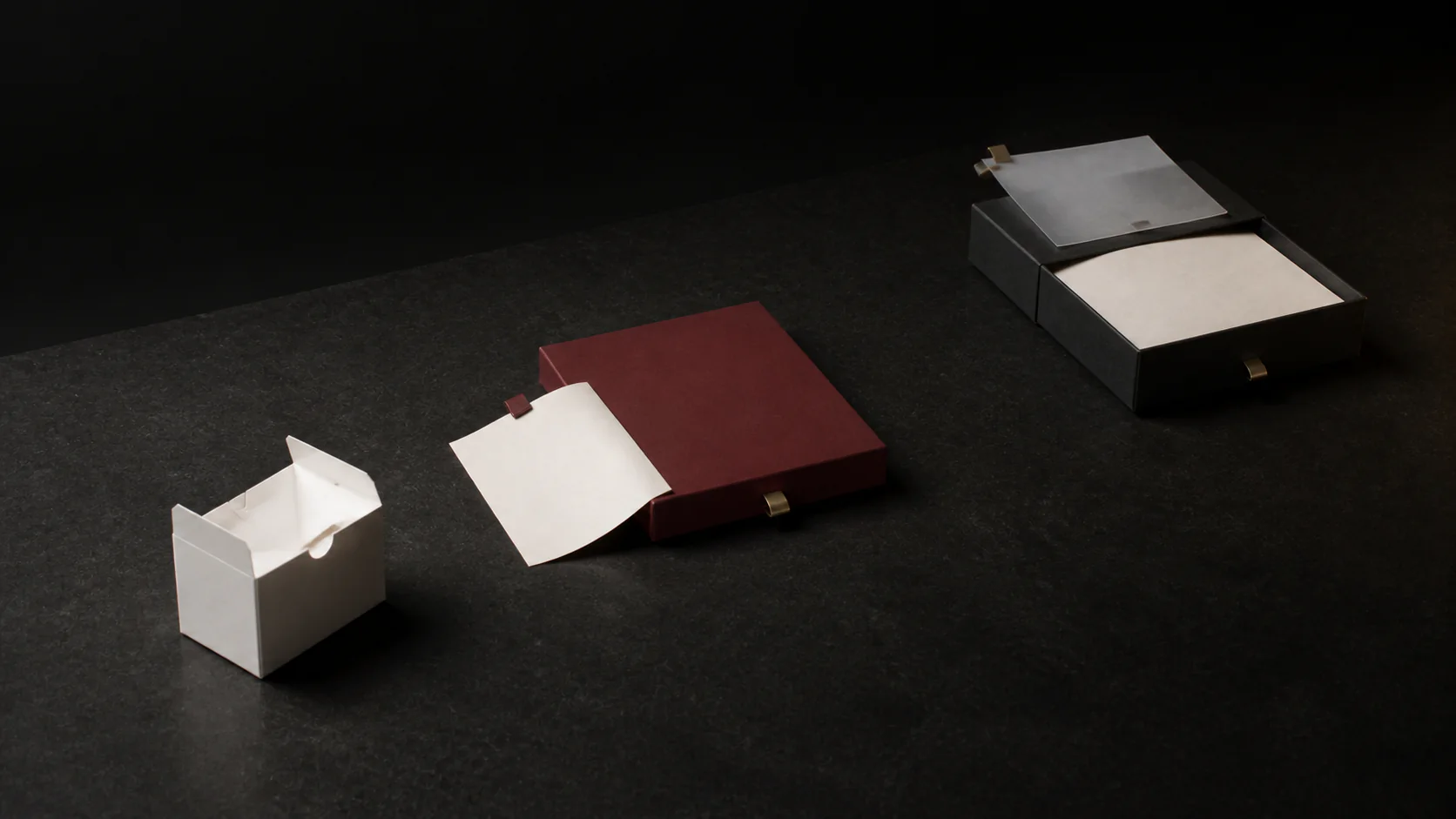 Illustrative sequence of three unbranded packaging prototypes on a dark mineral surface